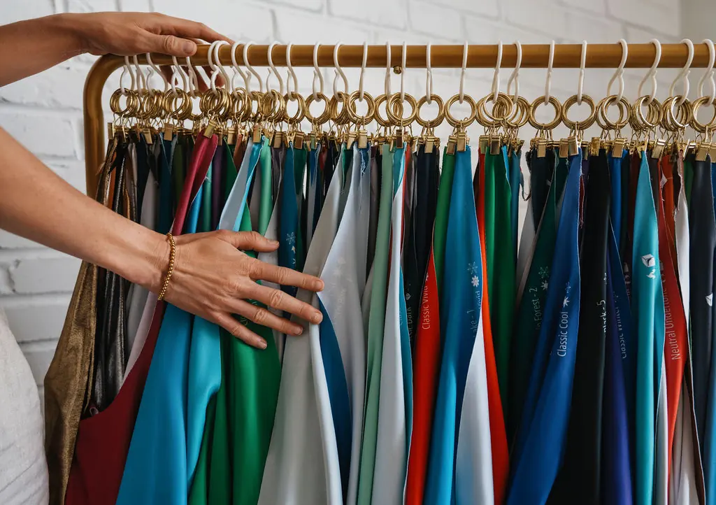 Hands sorting through a gold rack of labeled color analysis drapes in Kyshel's studio